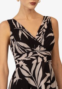 Robe noire avec corsage plissé, décolleté en V profond et motif de feuilles claires contrastant. Tissu lisse, taille cintrée et jupe fluide.