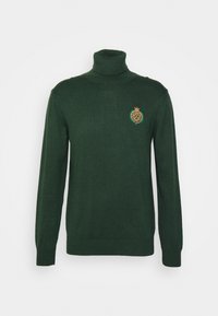 Grüner Rollkragenpullover aus Strickstoff. Mit einem goldenen und grünen gestickten Logo auf der Brust. Lange Ärmel und gerippte Bündchen.