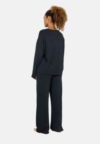 Top lungo oversized di colore blu navy scuro con maniche lunghe e pantaloni larghi in tessuto morbido. L'outfit presenta una vestibilità rilassata e un design minimalista.