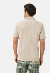 Beige polo met korte mouwen en een kraag, met een gladde textuur en subtiele stikdetails. Gecombineerd met groene en blauwe patroonshorts.
