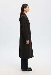 Mørkegrå koksgrå frakke med tynde striber, lang silhuet, med hakket revers og sidelommer, kombineret med mørke jeans og sorte sko.