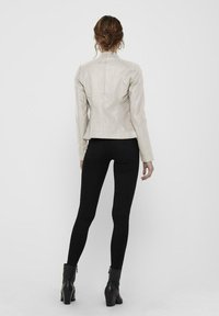 Giacca in pelle beige chiaro con un design aderente, maniche lunghe e colletto puntato. Abbinata a jeans skinny neri e stivali alla caviglia.