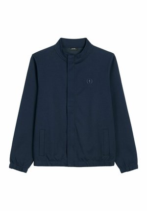 Granatowa kurtka zapinana na zamek z kołnierzem typu stójka, elastycznymi mankietami, dwoma przednimi kieszeniami z patkami oraz subtelnym, haftowanym logo na lewej piersi.