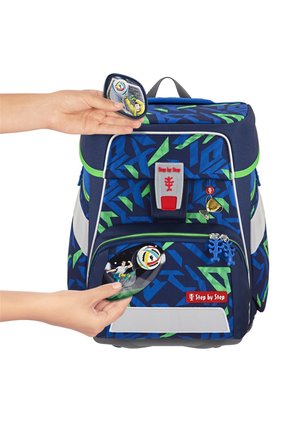 Zaino blu con motivi geometrici verdi. Caratterizzato da una tasca frontale con zip, un logo rosso e accessori removibili, tra cui distintivi e charm.