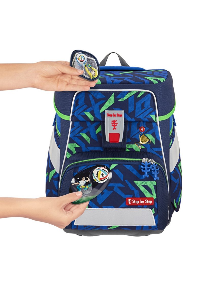 Zaino blu con motivi geometrici verdi. Caratterizzato da una tasca frontale con zip, un logo rosso e accessori removibili, tra cui distintivi e charm.