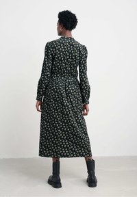 Langdurige zwarte jurk met bloemenpatroon, strakke taille, vloeiende rok. Draag met zwarte enkellaarzen, gestructureerde stof en een lichte glans.
