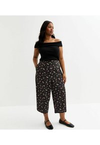 Svart off-the-shoulder ribbad topp som matchar högmidjade, vida byxor i svart tyg med rosa och vita blommönster. Platta svarta skor.