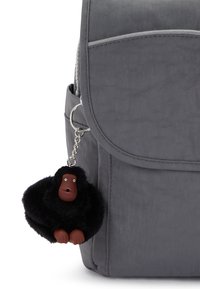 Sac à dos gris avec un porte-clés en forme de gorille noir et doux attaché. Le sac à dos comporte un rabat avant et une poche latérale.