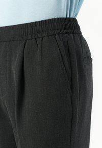 Pantalones negros de tejido texturizado con una cinturilla elástica y bolsillos laterales, con ligeros pliegues para un ajuste relajado.