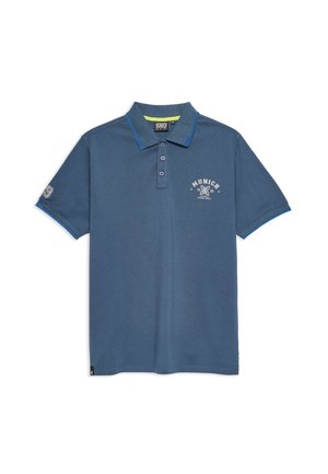 Polo de color azul oscuro hecho de una mezcla de algodón, con cuello, tapeta de tres botones y un estampado en el pecho que dice "Múnich 1939". Acentos azules en las mangas.