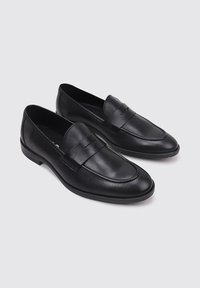 Mocasines de cuero negro con un acabado suave, que cuentan con una punta redondeada y una tira decorativa en la parte frontal. Tacón bajo y detalles mínimos.