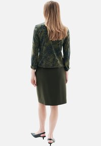 Blouse verte à manches longues avec un motif et des accents bleus, accompagnée d'une jupe crayon olive. Portée avec des chaussures à talons noires.