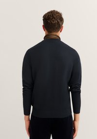 Maglione della marina con scollo rotondo, polsini e orlo a costine. Tessuto texturizzato su uno sfondo semplice.