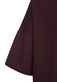 Bordeauxfarbenes, strukturiertes Oberteil mit lockeren, weiten Ärmeln. Der Stoff weist ein dezentes Kräuselungsmuster auf, das seine visuelle Tiefe und taktile Qualität verstärkt.