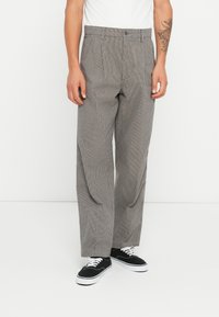 Gray checkered pants with a high-waisted design, featuring pleats and a relaxed fit. Worn with black sneakers. Textured fabric.