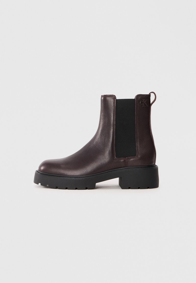 Bottine Chelsea en cuir brun foncé avec panneau latéral élastique noir, languette de tirage et semelle épaisse à crampons noire.