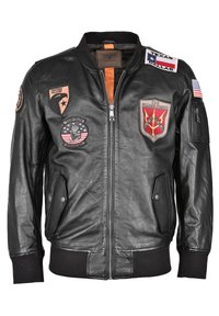 Svart läderbomberjacka med dragkedja, ribbade muddar och flera lappar med emblem och text, inklusive amerikanska flaggor och militära logotyper.