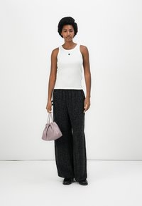 Débardeur blanc sans manches avec un petit logo, associé à un pantalon large noir à motif. Portant un sac à dos lilas avec cordon.