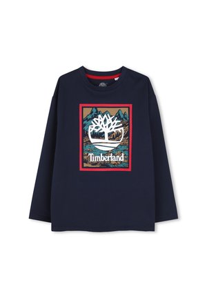 Chemise à manches longues bleu marine avec un grand logo Timberland représentant un arbre blanc au-dessus d’un paysage de montagne et de rivière dans un rectangle bordé de rouge.