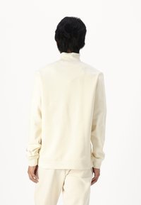 Felpa color crema a maniche lunghe con colletto alto, polsini aderenti e vestibilità comoda, realizzata in tessuto morbido e strutturato.