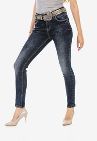 Dünne, dunkelblaue Jeans aus Denim mit einem ausgewaschenen Finish, ausgestattet mit einem dekorativen Gürtel mit Strasssteinen und eng anliegendem Schnitt an den Beinen.