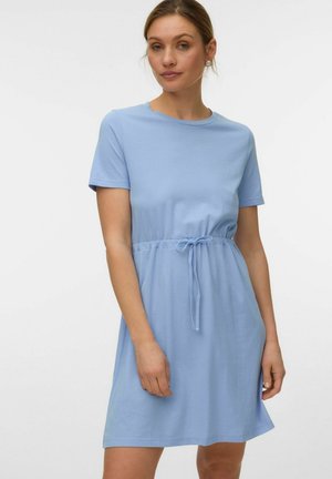 Woman wearing a light blue short-sleeve dress with a tie waist, standing against a plain white background.