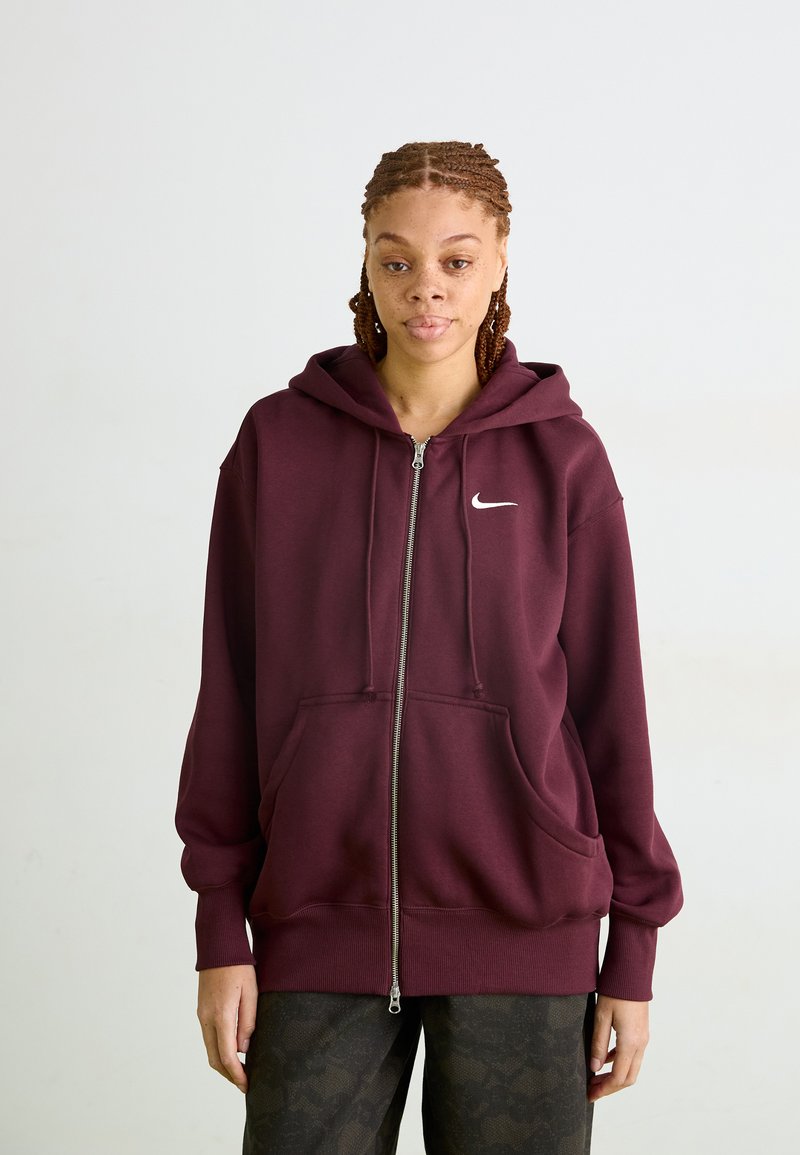 Corta-vento com fecho marrom, com bolsos frontais, capuz ajustável com cordão e logotipo da Nike em branco no lado esquerdo do peito, feito de tecido macio.