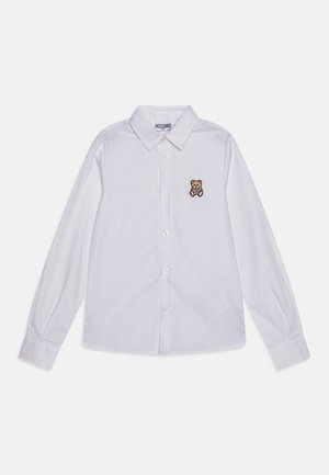 Camisa blanca de manga larga y botones con cuello puntiagudo, que presenta un pequeño bordado de un oso de peluche marrón en el lado izquierdo del pecho.