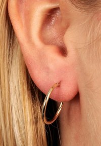 Gul hoops ørehänge i nærbillede, der har en glat, skinnende overflade og et cirkulært design, båret i et gennemhullet øre.