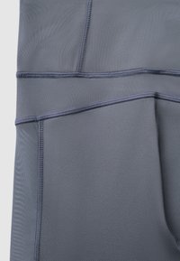 Gros plan sur un tissu gris foncé lisse avec des coutures détaillées et des lignes de couture visibles sur un vêtement de sport.