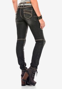 Schwarze Skinny-Jeans aus Denim mit kontrastierenden goldenen Nähten, ausgestattet mit zwei Gesäßtaschen und einer niedrigen Taille. Dazu kombiniert braune High-Heels.