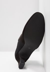 Talons en daim noir avec une semelle en caoutchouc texturée. Taille 37 indiquée sur la face inférieure. Design à talon effilé avec tissu élastique.