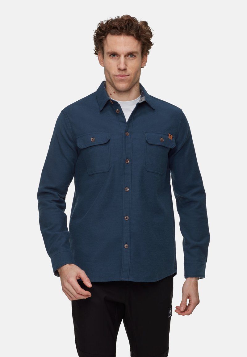 Camicia button-up blu scuro con due taschini sul petto, bottoni marroni e colletto. Tessuto morbido con una vestibilità rilassata e orlo arrotondato.