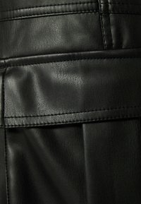 Svart konstläder med en texturerad yta. Synlig sömnad och en vikt detalj skapar ett strukturerat designelement.