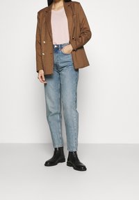 Brun rutig kavaj med dubbla knappar, ljusrosa t-shirt, ljusblå raka jeans och svarta ankelstövlar.