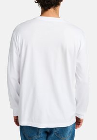 Long-sleeve white t-shirt made of cotton, featuring a relaxed fit, crew neck, and plain back with no visible patterns or designs.