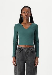 Grønn, ribbet langermet crop-top med V-halsdesign, sammen med høytekkede, lysegrå denim. Enkel, tettsittende silhuett.