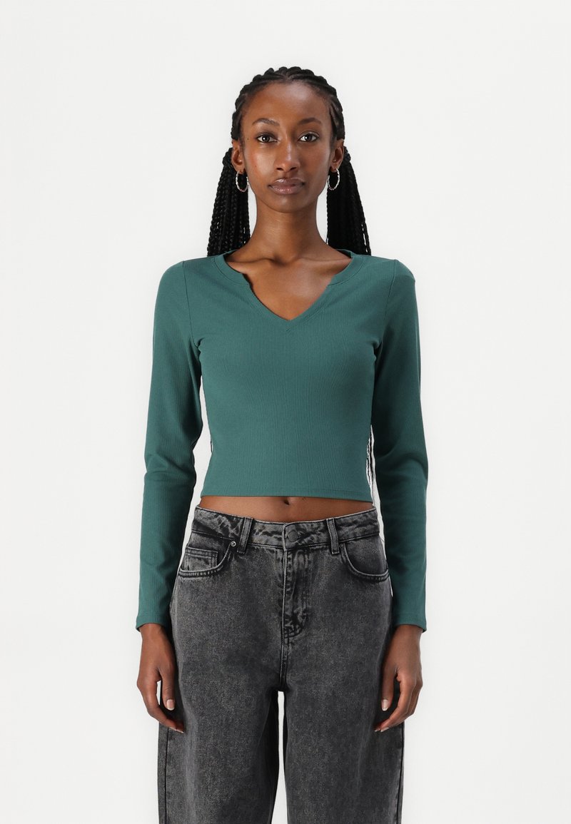 Grønn, ribbet langermet crop-top med V-halsdesign, sammen med høytekkede, lysegrå denim. Enkel, tettsittende silhuett.