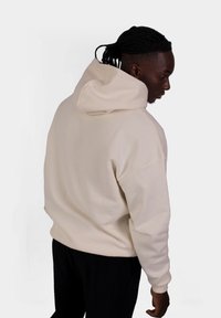 Felpa con cappuccio beige, dal taglio morbido e rilassato, con spalle drop. Presenta un cappuccio grande e un design minimalista.