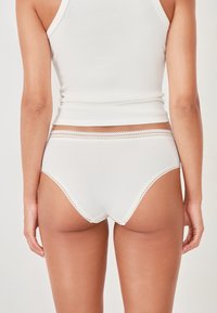 Mutande in cotone a coste bianche con bordo in pizzo ondulato in vita, caratterizzate da un design senza cuciture e una texture liscia.