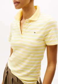 Gul og hvid stribet polo-shirt med spredt krave, korte ærmer og et lille logo på brystet. Lavet af textured stof.