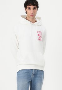Witte hoodie met een kangoeroezak, voorzien van een roze grafische print op de linkerkant van de borst. Met een trekkoord in de capuchon en geribde manchetten. Gemaakt in combinatie met lichtblauwe jeans.