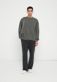 Tmavě šedá mikina s kulatým výstřihem, spárovaná s volnými kalhotami ve stejném odstínu. Bílá sneakers a malá šedá kabelka přes rameno dokončují vzhled.