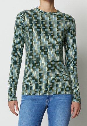 Long-sleeve shirt with green, blue, and beige geometric vertical bar pattern worn with light blue jeans.