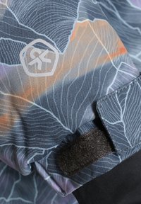 Tkanina s vzorom, ki prikazuje sivo in belo zasnovo listov z oranžnimi poudarki. Vključuje logo in detajl črne Velcro zaponke.