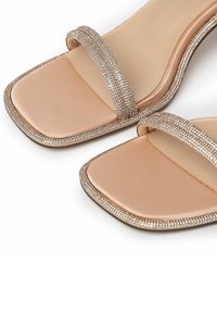 Nude satijnen slidesandalen met dubbele banden versierd met kleine rhinestones, vierkante neus en een gladde, gestructureerde inlegzool. Vlakke zool.