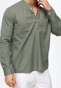 Camisa de manga larga color verde oliva con cuello en muesca y tapeta de botones, que presenta una textura suave y un diseño ajustado.