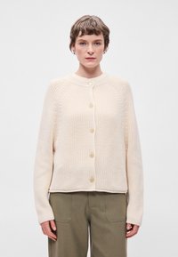 Κρεμ πλεκτό ζακέτα με στρογγυλή λαιμόκοψη, που διαθέτει κλείσιμο με κουμπιά και ραβδωτές λεπτομέρειες στα μανίκια και το στρίφωμα. Υφασμα με υφή.