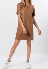 Robe shift en suede marron avec des manches courtes, un col rond doté d'une découpe en forme de serrure, et des détails de couture verticaux. Portée avec des baskets blanches.