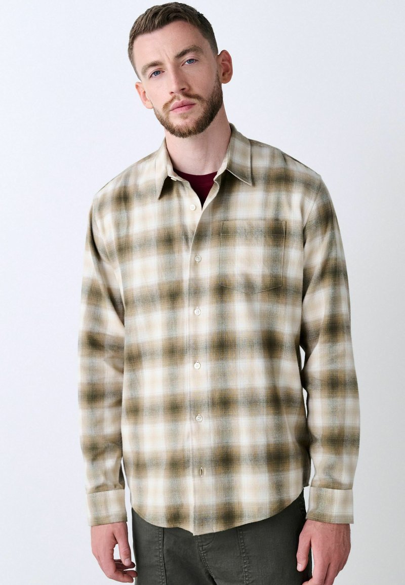 Camicia in flanella a quadri beige e marrone, con bottoni davanti, taschino sul petto e maniche lunghe. Morbido al tatto, orlo curvo.